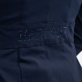 Seitliches Detailbild der Rückseite des Harcour Turnierjackets Oria in Navy. Im Bereich der Taille betont ein angedeuteter Bund den femininen Schnitt der Turnierjacke für Damen. Ein funkelnder Harcour-Logo-Schriftzug aus großen, auberginefarbenen Strasssteinen ziert diesen Taillenbund. Dieses wunderschöne Glitzerdetail wertet die dezente Rückansicht auf und macht das Reitsakko für Markenfans zu einem echten Designerstück, das die weibliche Silhouette im Turniersport elegant in Szene setzt.