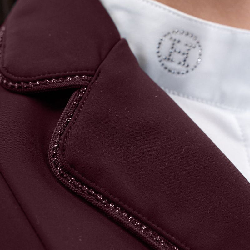 Hochauflösende Detailaufnahme der rechten Kragenseite des Harcour Damen Turnierjackets Oria in Aubergine. Die elegant abgerundeten Kragenkanten und die rahmende Glitzerlitze am Kragenrand harmonieren perfekt mit dem weichen, leichten Material der Turnierreitjacke. Diese verspielten Design-Details machen die funktionale Harcour Turnierkleidung zum echten Blickfang. Ideal einsetzbar als exklusives Allround-Turniersakko, edles Dressurjacket oder funktionales Springturnierjacket für Frauen.