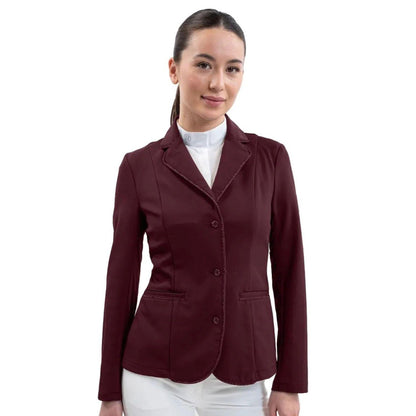 Eine Turnierreiterin präsentiert das feminine Harcour Damen Turnierjacket Oria in Aubergine, einem luxuriösen, dunkelroten Farbton, der Violett- und Brauntöne elegant vereint. Das figurbetonte Reitsakko mit hochelastischem Harcour-Riders-Stretch wird mit weißem Harcour Turniershirt und weißer Turnierreithose kombiniert. Die rahmende Glitzerlitze von Kragen bis Saum, betonte vordere Einschubtaschen sowie mit Kristallsteinen verzierte Knöpfe an Ärmeln und Verschluss machen die Reitjacke zum Blickfang.