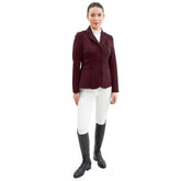 Eine Turnierreiterin präsentiert ein komplettes Harcour Turnieroutfit. Sie trägt das Damen Turnierjacket Oria in Aubergine, kombiniert mit weißer Turnierreithose und dem Harcour Turniershirt Shine mit weißem Latz. Dieses edle Reitsakko setzt optische Highlights und bietet maximale Sicherheit: Es ist kompatibel mit dem Harcour Ouraye HIT AIR Airbag und allen Airbagwesten, die unter der Turnierkleidung getragen werden. Ein elegantes und sicheres Reitoutfit für den anspruchsvollen Turniersport.