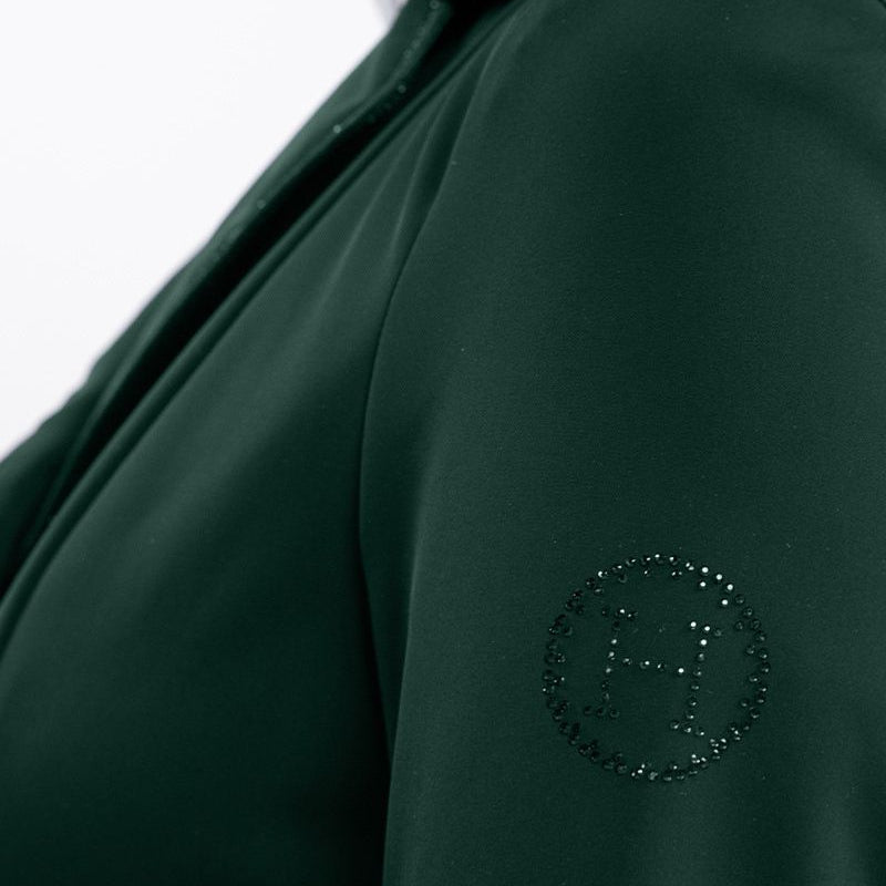 Detailansicht des linken Ärmels des Harcour Oria Jungle Damen Turnierjackets mit dem runden, durch Strasssteine und Glitzer verzierten Harcour-Logo, passend zur dunkelgrünen Grundfarbe des Turniersakkos. Raffiniertes Glitzer-Detail in dezenter Eleganz.