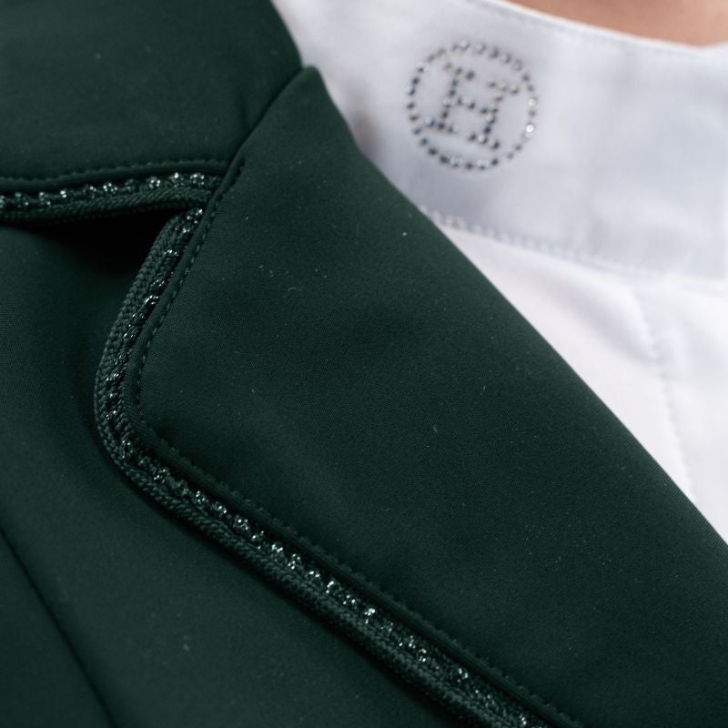 Hochauflösende Detailaufnahme der rechten Kragenseite des Harcour Damen Turnierjackets Oria in Jungle. Die elegant abgerundeten Kragenkanten und die rahmende Glitzerlitze am Kragenrand harmonieren perfekt mit dem weichen, leichten Material der Turnierreitjacke. Diese verspielten Design-Details machen die funktionale Harcour Turnierkleidung zum echten Blickfang. Ideal einsetzbar als exklusives Allround-Turniersakko, edles Dressurjacket oder funktionales Springturnierjacket für Frauen.