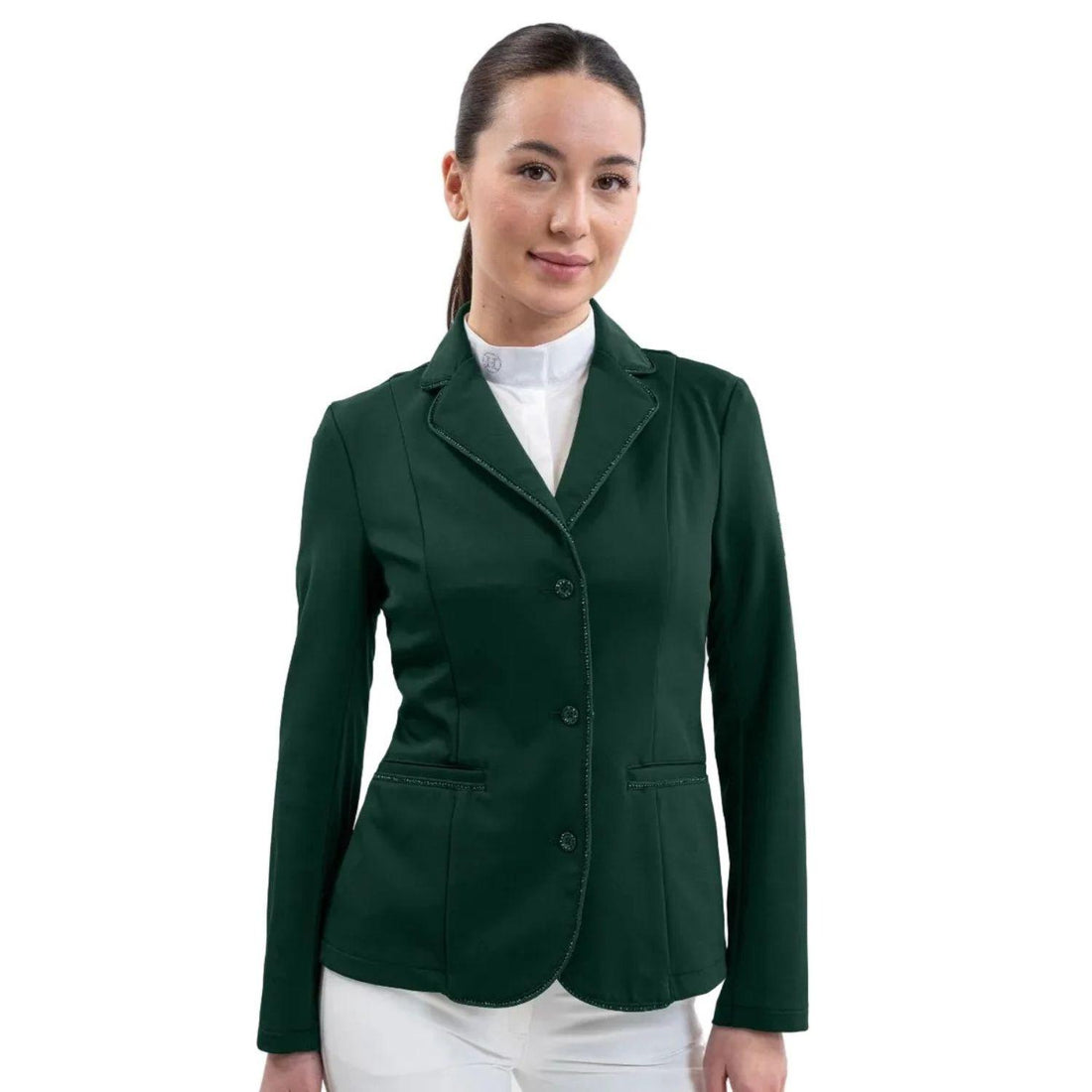 Eine Turnierreiterin präsentiert das feminine Harcour Damen Turnierjacket Oria in Jungle, einem luxuriösen, dunkelgrünen Farbton. Inspiert durch die Farben des Dschungels. Das figurbetonte Reitsakko mit hochelastischem Harcour-Riders-Stretch wird mit weißem Harcour Turniershirt und weißer Turnierreithose kombiniert. Die rahmende Glitzerlitze von Kragen bis Saum, betonte vordere Einschubtaschen sowie mit Kristallsteinen verzierte Knöpfe an Ärmeln und Verschluss machen die Reitjacke zum Blickfang.