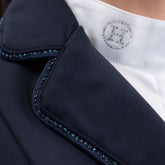 Hochauflösende Detailaufnahme der rechten Kragenseite des Harcour Damen Turnierjackets Oria in Navy. Die elegant abgerundeten Kragenkanten und die rahmende Glitzerlitze am Kragenrand harmonieren perfekt mit dem weichen, leichten Material der Turnierreitjacke. Diese verspielten Design-Details machen die funktionale Harcour Turnierkleidung zum echten Blickfang. Ideal einsetzbar als exklusives Allround-Turniersakko, edles Dressurjacket oder funktionales Springturnierjacket für Frauen.