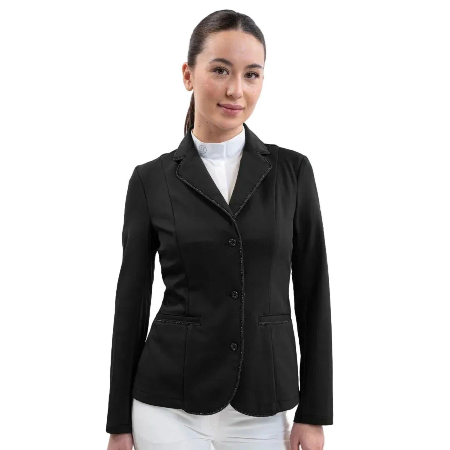 Eine Turnierreiterin präsentiert das feminine Harcour Damen Turnierjacket Oria in Schwarz, der klassischsten Farbe im Reitsport. Das figurbetonte Reitsakko mit hochelastischem Harcour-Riders-Stretch wird mit weißem Harcour Turniershirt und weißer Turnierreithose kombiniert. Die rahmende Glitzerlitze von Kragen bis Saum, betonte vordere Einschubtaschen sowie mit Kristallsteinen verzierte Knöpfe an Ärmeln und Verschluss machen die Reitjacke zum Blickfang.