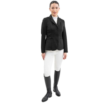 Eine Turnierreiterin präsentiert ein komplettes Harcour Turnieroutfit. Sie trägt das Damen Turnierjacket Oria in ASchwarz, kombiniert mit weißer Turnierreithose und dem Harcour Turniershirt Shine mit weißem Latz. Dieses edle Reitsakko setzt optische Highlights und bietet maximale Sicherheit: Es ist kompatibel mit dem Harcour Ouraye HIT AIR Airbag und allen Airbagwesten, die unter der Turnierkleidung getragen werden. Ein elegantes und sicheres Reitoutfit für den anspruchsvollen Turniersport.