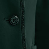 Detailaufnahme der Vorderseite mit dem edlen Knopfverschluss der Harcour Damen Turnierreitjacke Oria in Jungle. Das Bild zeigt das harmonische Zusammenspiel der mit Kristallsteinen veredelten Knöpfe und der funkelnden Glitzerlitze, die das Reitsakko vom Kragen bis zum Saum rahmt. Diese hochwertige Verarbeitung der sichtbaren Knöpfe über dem Double-Closure-System ist eine Besonderheit der Turnierbekleidung für Reiterinnen, die ein exklusives und individuelles Turnieroutfit suchen.