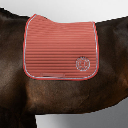 Harcour Schabracke Karembar Aurora Pink auf dunkelbraunen Pferd mit dunkelbraunem Langhaar (typische leichte Farbveränderungen im Kurzhaar sichtbar). Die Dressurschabracke zeigt den anatomischen Schnitt für perfekte Sattellage, die horizontale Steppung und die glitzernde silberne Litze im Detail. Das Harcour-Logo ist silber eingestickt. Ein weicher, warmer Kontrast: Das frische Rosa bildet wunderschönen Gegenpol zum tiefen, dunklen Fell. hochfunktionale Sattelunterlage mit Glitzer für Training und Turnier.
