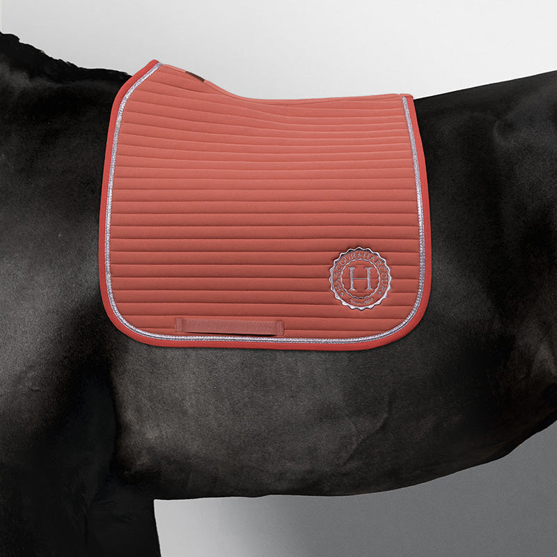 Harcour Schabracke Karembar Aurora Pink auf einem schwarzen Pferd. Die leuchtende rosa Dressurschabracke zeigt den anatomischen Schnitt für optimale Widerristfreiheit und die charakteristische horizontale Steppung. Die silberne Glitzer-Litze bildet einen eleganten Akzent. Ein atemberaubender Kontrast: Das helle Aurora Pink "poppt" dramatisch gegen das tiefe Schwarz des Pferdes und das schwarze Langhaar. Diese moderne Schabracke mit Glitzer für Pferde ist ein echter rendsetter im Dressurviereck.