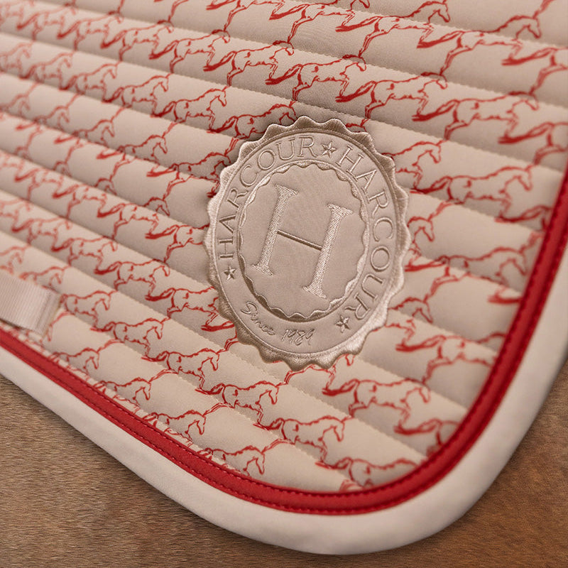 Detail der Harcour Schabracke Karembar Jump Shell Grapefruit: Horizontale Steppung, helles Einfassband in Beige und korallfarbene Litze passend zum Pferdeprint. Das runde Harcour Logo Batch in Shell sorgt für einen stylischen Auftritt im Spring-, Dressur- oder Ponysattel.