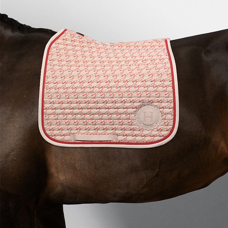 Harcour Dressur-Schabracke Karembar Jump Shell Grapefruit auf einem dunkelbraunen Pferd. Die warme Beige-Grundfarbe (Shell) und die korallefarbene (Grapefruit) flache Litze setzen einen sportlichen Akzent zum dunkelbraunen Kurzhaar und Langhaar. Der anatomische Schnitt und die horizontale Steppung sind gut sichtbar. Perfekt für das Dressurviereck.