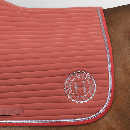 Größerer Bildausschnitt der gesamten hinteren Hälfte der Harcour Schabracke Karembar in Aurora Pink. Diese Ansicht zeigt die makellose Verarbeitung der horizontalen Steppung und das harmonische Zusammenspiel der Materialien. Deutlich zu erkennen ist das kräftiger rosa abgesetzte Einfassband, das einen edlen Kontrast zur helleren Sattelunterlage bildet. Die silberne, flache Glitzer-Litze verläuft parallel zur Einfassung und verleiht der Schabracke ihre besondere Eleganz. 