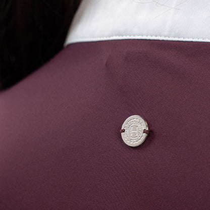 Die Rückansicht des Harcour-Turniershirts Shine aubergine, einem dunklen Violettton, mit dem dezenten, runden, silbernen Logo auf dem elastischen Stretchmaterial für optimale Bewegungsfreiheit. Der darüber liegende Stehkragen ist kontrastfarbig in Weiß abgesetzt. 