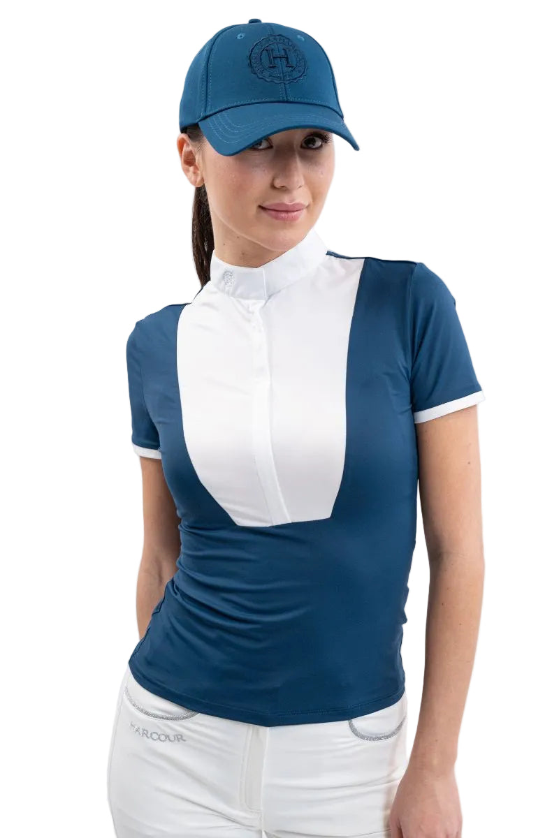 Eine Großaufnahme einer Turnierreiterin zeigt das figurbetonte Harcour Kurzarm-Turniershirt Shine in der aquamarin-türkisen Farbe Blue Lagoon (Petrol), welches durch sein leichtes, atmungsaktives Material ideal für den Reitsport im Sommer geeignet ist und mit seinem weißen Latz sowie Stehkragen einen eleganten Kontrast zur weißen Harcour Turnierreithose bildet.