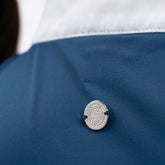 Die Rückansicht des Harcour Turniershirts Shine Blue Lagoon mit dem dezenten, runden, silbernen Logo auf dem elastischen Stretchmaterial für optimale Bewegungsfreiheit. Der darüber liegende Stehkragen ist kontrastfarbig in Weiß abgesetzt. 