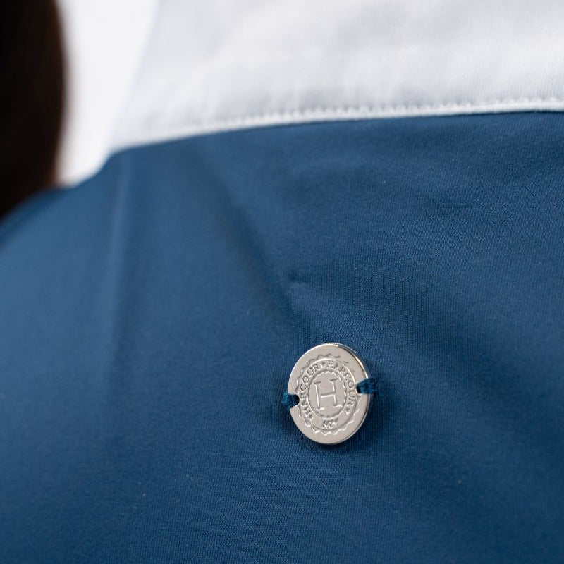 Die Rückansicht des Harcour Turniershirts Shine Blue Lagoon mit dem dezenten, runden, silbernen Logo auf dem elastischen Stretchmaterial für optimale Bewegungsfreiheit. Der darüber liegende Stehkragen ist kontrastfarbig in Weiß abgesetzt. 