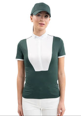 Eine Turnierreiterin trägt frontal das figurbetonte Harcour Turniershirt Shine in Jungle, bei dem der edle weiße Latz und der funkelnde Stehkragen mit Kristall-Logo einen klassischen Kontrast für das Dressurviereck bilden.