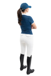 Die Rückansicht zeigt eine Turnierreiterin im eleganten Harcour Turniershirt Shine kombiniert mit weißer Reithose und Reitstiefeln, wobei das französische Design mit besonderer Raffinesse und Funktionshighlights für absoluten Tragekomfort im Sattel sorgt. Sehr femininier und körpernaher Schnit.