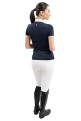 Die Rückansicht zeigt eine Turnierreiterin im eleganten Harcour Turniershirt Shine kombiniert mit weißer Reithose und Reitstiefeln, wobei das französische Design mit besonderer Raffinesse und Funktionshighlights für absoluten Tragekomfort im Sattel sorgt.