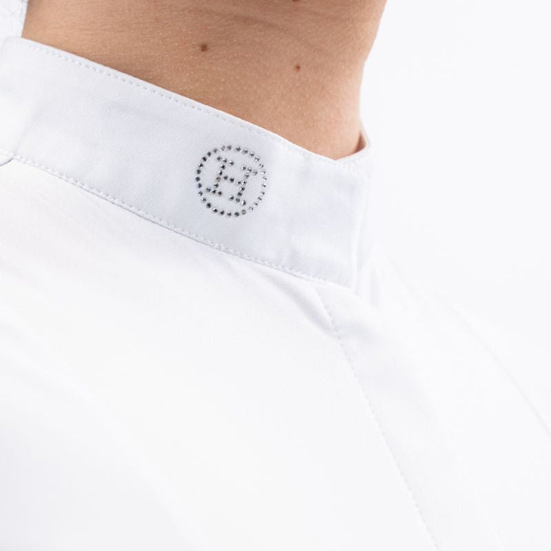 Eine Nahaufnahme des eleganten weißen Stehkragens am Harcour Damen Turniershirt Shine White zeigt das funkelnde H-Logo aus hellen Kristallsteinen, welches unter dem Turnierjacket oder Dressurfrack für einen raffinierten Hauch von Glitzer sorgt und ein zusätzliches Plastron überflüssig macht. Verschluss durch einen Magneten und langen Reißverschluss zum An- und Ausziehen. 