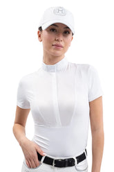 Eine Turnierreiterin präsentiert das weiße Harcour Kurzarm-Turniershirt Shine, das durch einen figurbetonten, femininen Schnitt und einen dezenten, gleichfarbigen Latz als elegantes Zierdetail besticht. Das atmungsaktive und leichtgewichtige Stretchmaterial sorgt für höchsten Tragekomfort beim Reiten im Sommer und macht das Shirt, kombiniert mit einer weißen Harcour Turnierreithose für einen strahlenden und neutralen Auftritt, zur perfekten Wahl für einen professionellen Look unter Turnierjackets.