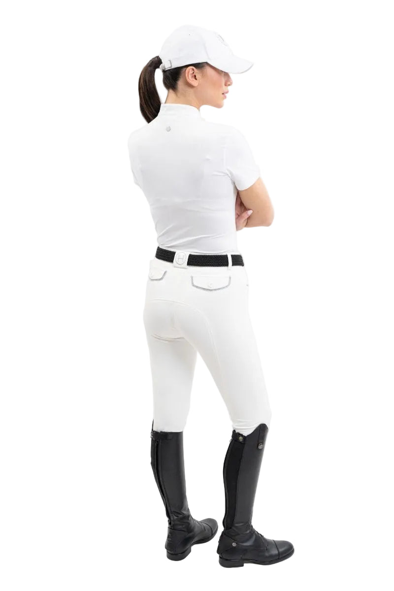 Die Rückansicht zeigt eine Turnierreiterin im eleganten Harcour Turniershirt Shine in der Farbe White kombiniert mit weißer Reithose und Reitstiefeln, wobei das französische Design mit besonderer Raffinesse und Funktionshighlights für absoluten Tragekomfort im Sattel sorgt.