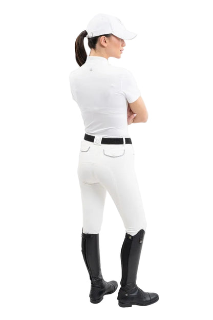 Die Rückansicht zeigt eine Turnierreiterin im eleganten Harcour Turniershirt Shine in der Farbe White kombiniert mit weißer Reithose und Reitstiefeln, wobei das französische Design mit besonderer Raffinesse und Funktionshighlights für absoluten Tragekomfort im Sattel sorgt.