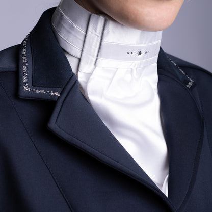Weißes Harry’s Horse Plastron Diamond, getragen über einem Turniershirt und perfekt eingepasst in den V-Ausschnitt eines blauen Turnierjackets. Die hellen Glitzersteine am Kragen funkeln im Sonnenlicht, während das vorgebundene Plastron im Nacken per Klettverschluss einfach geschlossen wird.