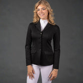 Reiterin im klassischen schwarzen Harry’s Horse Turnierjacket Competition kombiniert mit weißer Turnierreithose und Turniershirt. Das Tragefoto zeigt die feminine, taillierte Passform der eleganten Turnierjacke sowie die 4-Knopf-Leiste und Klapptaschen im kompletten Turnieroutfit.