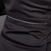 Makro-Detailaufnahme des Gürtelbands in Taillenhöhe auf der Rückseite des schwarzen Harry’s Horse Turnierjackets Glitter. Die taillierte Form des Reitsakkos wird durch eine mittig verlaufende graue Glitzerbiese betont, die oben und unten von präzise eingefassten, kleinen schwarzen Strasssteinen gerahmt ist. Am unteren Bildrand zeichnen sich zudem die dezent verzierten Ansätze der Gehschlitze des elastischen Stretch-Sakkos ab.
