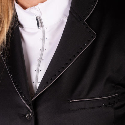 Nahaufnahme der edlen Verarbeitungsdetails des schwarzen Harry’s Horse Turnierjackets Glitter. Zu sehen sind der Kragen und das Revers des Reitsakkos, umrahmt von einer kontraststarken grauen Glitzerbiese und einer Reihe feiner schwarzer Strasssteine. Auch die Brusttasche auf der linken Seite greift das funkelnde Design mit Glitzerbiese und Strass-Akzenten auf. Darunter wird eine weiße Turnierbluse mit Stehkragen getragen, die den luxuriösen Gesamteindruck unterstreicht.