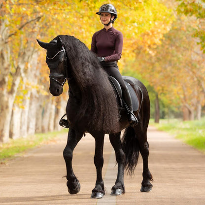 Harmonisches Reitoutfit in Schwarz: Eine Reiterin auf einem Friesen (Rappe) im kompletten LeMieux Essence Dressurset. Das Pferd trägt die schwarze Essence Dressurschabracke und die passende schwarze Essence Fliegenmütze (Fliegenhaube). Dieses dezente, elegante Set ist ideal für das Training oder Reitlehrgänge und besticht durch zeitlose Ästhetik.
