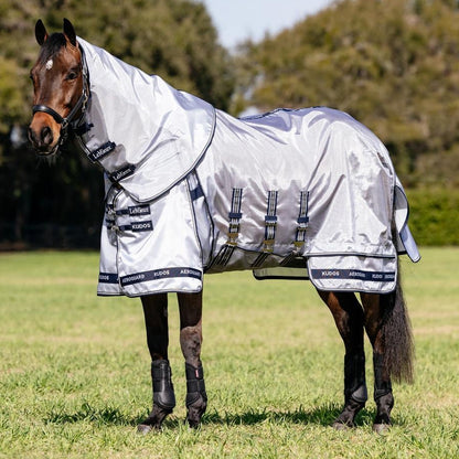 Ein Pferd trägt die silberne LeMieux Fliegendecke Kudos AeroGuard inklusive Halsteil entspannt auf der Weide. Das extrem leichte, atmungsaktive Ripshield-Mesh-Material glänzt im Sonnenlicht, reflektiert das Sonnenlicht und staut so keine Hitze unter der Sommerdecke.