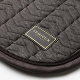 Nahaufnahme der LeMieux Heritage Dressurschabracke in Cocoa: Edles LeMieux Heritage Logo-Badge mit goldener Schrift auf Fischgrät-Chevron-Steppung, veredelt durch eine dunkelbraune Velours-Einfassung und zweifarbige Zierkordeln.