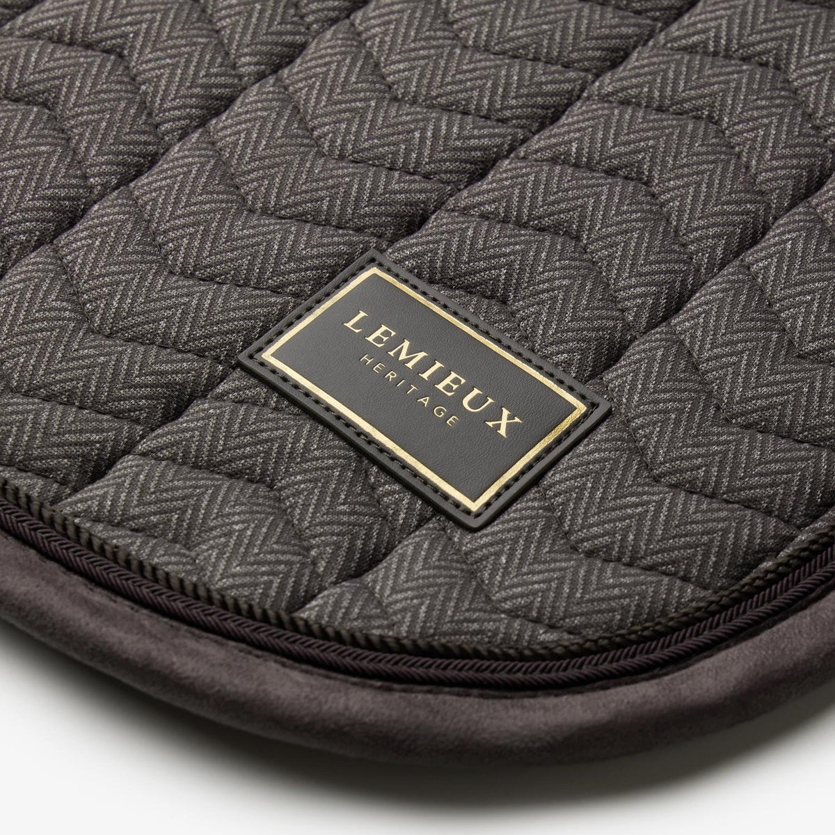 Nahaufnahme der LeMieux Heritage Dressurschabracke in Cocoa: Edles LeMieux Heritage Logo-Badge mit goldener Schrift auf Fischgrät-Chevron-Steppung, veredelt durch eine dunkelbraune Velours-Einfassung und zweifarbige Zierkordeln.