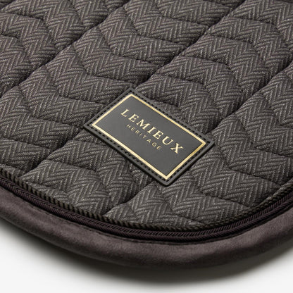 Nahaufnahme der LeMieux Heritage Dressurschabracke in Cocoa: Edles LeMieux Heritage Logo-Badge mit goldener Schrift auf Fischgrät-Chevron-Steppung, veredelt durch eine dunkelbraune Velours-Einfassung und zweifarbige Zierkordeln.