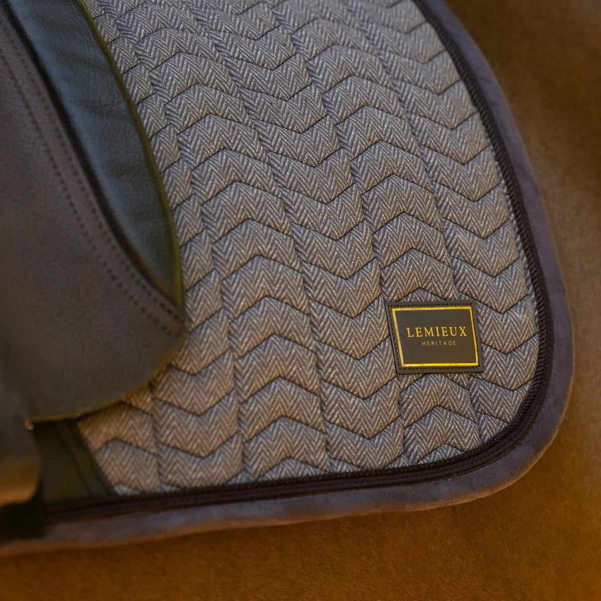 Die braune LeMieux Heritage Dressurschabracke Herringbone Cocoa im Einsatz unter dem Dressursattel: Perfekte Passform am Pferderücken mit eleganter Chevron-Fischgrät-Steppung, stoßdämpfender Velours-Einfassung und sichtbarem LeMieux Heritage Emblem.