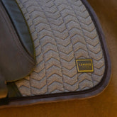 Die braune LeMieux Heritage Dressurschabracke Herringbone Cocoa im Einsatz unter dem Dressursattel: Perfekte Passform am Pferderücken mit eleganter Chevron-Fischgrät-Steppung, stoßdämpfender Velours-Einfassung und sichtbarem LeMieux Heritage Emblem.