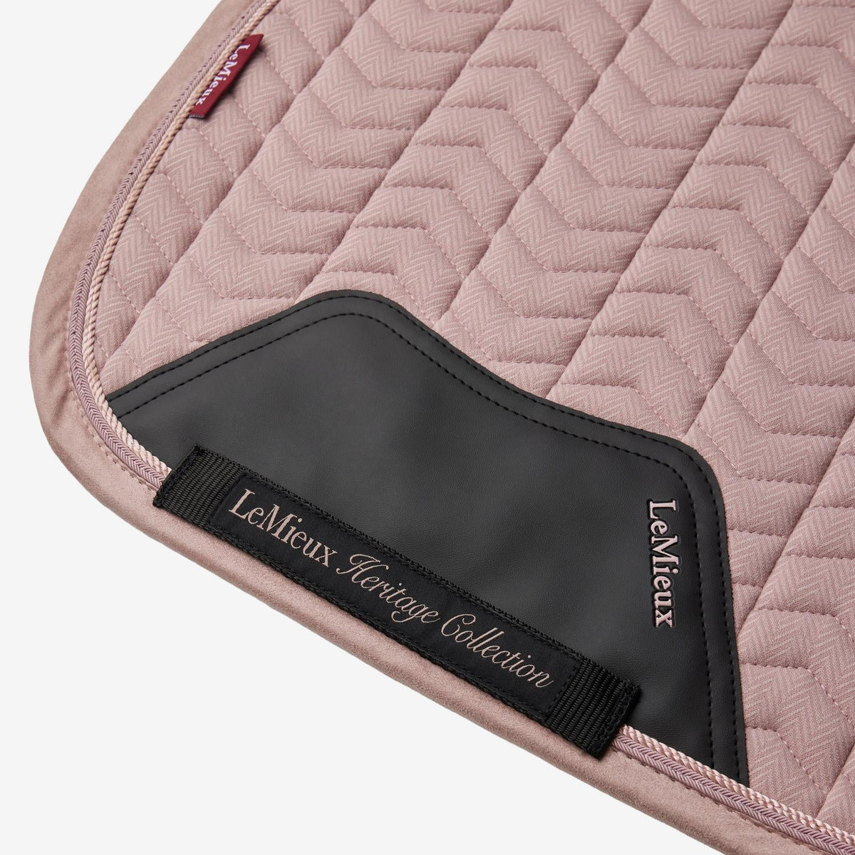 Detailaufnahme des patentierten Gurtschutzbereichs der LeMieux Heritage-Dressurschabracke in Wild Rose (Altrosa). Zu sehen sind die strapazierfähige PU-Leder-Verstärkung zum Schutz vor Abrieb, das bestickte Gurtband der LeMieux Heritage Collection mit verdeckten Schlaufen des Gurtverriegelungssystems sowie die zweifache Zierkordel an der Velours-Einfassung.