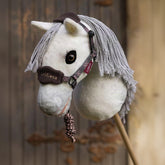 Das weiße LeMieux Hobby Horse Coco als Fliegenschimmel vor einem rustikalen Stalltor, ausgestattet mit dem Heritage Vogue Halfter und Führstrick in Cocoa mit braunem Karomuster für vielseitiges Hobbyhorsing und stilechte Pferdepflege.