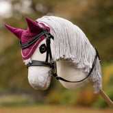 Die violette LeMieux Hobby Horse Fliegenmütze Blackberry getragen auf dem Kopf des LeMieux Steckenpferd Coco (schneeweißer Schimmel) in Kombination mit der LeMieux Hobby Horse Trense Competition. Die dunkelviolette Fliegenhaube setzt in herbstlicher Kulisse, beim Hobby-Horse-Training sowie auf Turnieren edle Akzente auf hellen und dunklen Hobby Horses.
