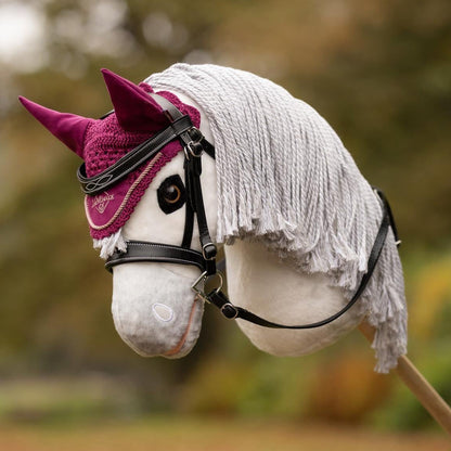 Die violette LeMieux Hobby Horse Fliegenmütze Blackberry getragen auf dem Kopf des LeMieux Steckenpferd Coco (schneeweißer Schimmel) in Kombination mit der LeMieux Hobby Horse Trense Competition. Die dunkelviolette Fliegenhaube setzt in herbstlicher Kulisse, beim Hobby-Horse-Training sowie auf Turnieren edle Akzente auf hellen und dunklen Hobby Horses.