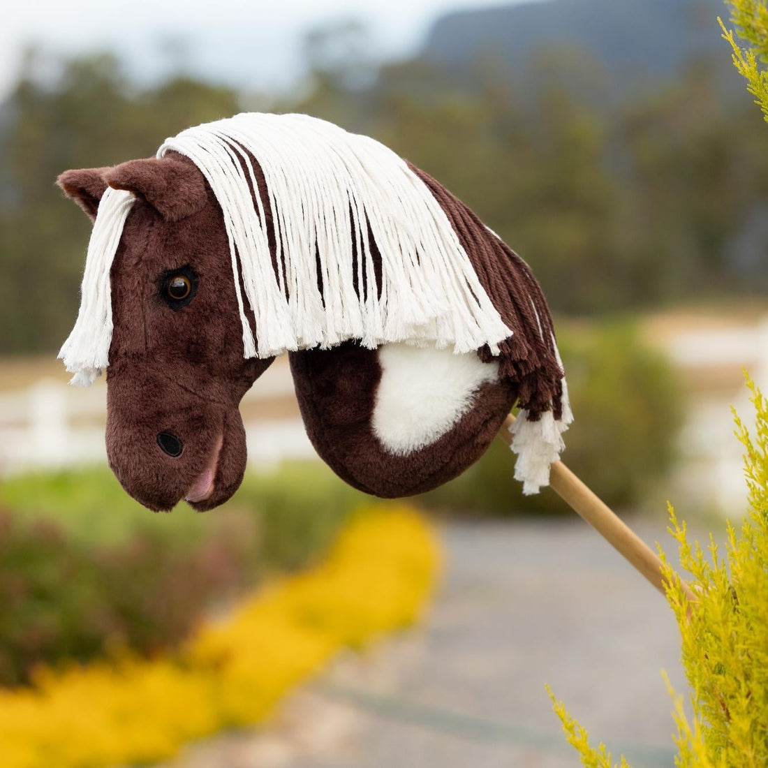 Das LeMieux Hobby Horse Dazzle als detailgetreues Paint Horse im Outdoor-Einsatz auf dem Reitplatz: Ein realistisches braun-weißes Steckenpferd für Kinder und Turnierreiter zum Trainieren von Parcours, Dressur und Westernreiten. 