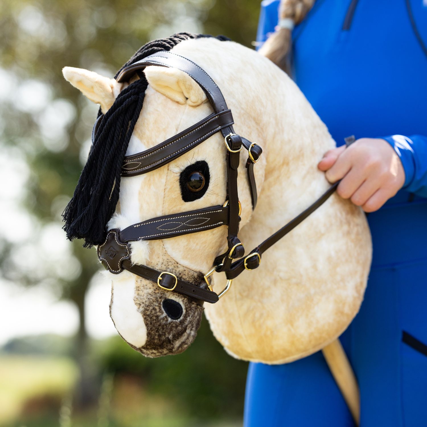 Ein Mädchen trainiert beim Springen mit dem LeMieux Steckenpferd Hobby Horse Dream und hält die Zügel fest in der Hand. Das Pferd trägt als perfektes Zubehör die LeMieux Hobby Horse Trense Grackle aus braunem Leder. Mit diesem realistischen Reitsport-Zubehör, das an alle LeMieux Hobby Horses passt, verleihst du deinem Steckenpferd ein individuelles und authentisches Äußeres.