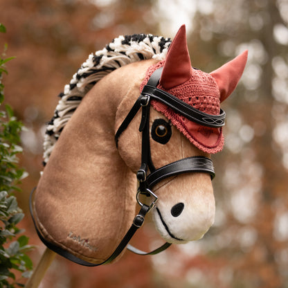 Die rosafarbene LeMieux Hobby Horse Fliegenhaube Spiced Earth auf dem Fjordpferd-Steckenpferd Oskar. Kombiniert mit der schwarzen Hobby Horse Trense Competition in herbstlicher Outdoor-Umgebung – perfektes Zubehör für Hobby Horsing Turniere, Training und Ausritte.