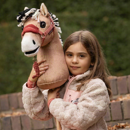 Nahaufnahme: Mädchen hält das LeMieux Hobby Horse Oskar (norwegisches Fjordpferd als Steckenpferd) im Arm. Das Falbe-Pony mit zweifarbiger Stehmähne, Mehlmaul und bernsteinfarbenen Augen trägt das LeMieux Hobby-Horse-Halfter mit Führstrick in Spiced Earth.