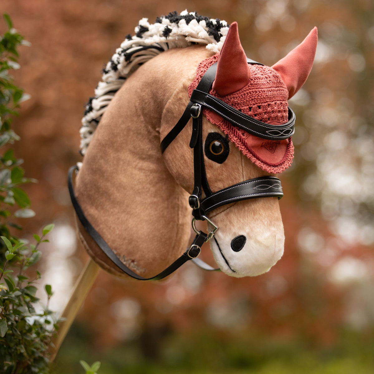 LeMieux Hobby Horse Oskar (Fjordpferd Falbe), getrenst mit der schwarzen LeMieux Hobby Horse Trense Competition und der gehäkelten Fliegenmütze in Spiced Earth. Realistisches Steckenpferd mit zweifarbiger Stehmähne für das Hobbyhorsing.
