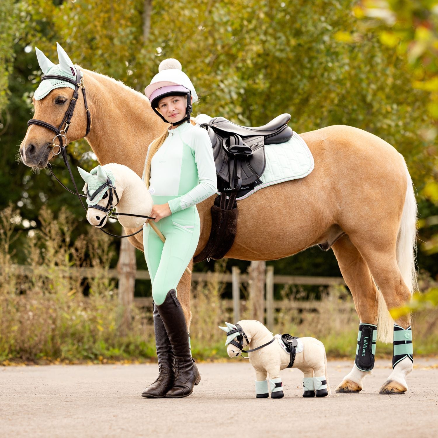 Das LeMieux Hobby Horse Popcorn in Palomino mit Blesse ist dem echten Pony von Influencerin Harlow nachempfunden. Die Influencerin hält das Hobby Horse Popcorn in der Hand. Auf dem Bild steht die passende LeMieux Toy Pony Ausgabe von Popcorn direkt daneben auf dem Boden