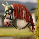 Das LeMieux Hobby Horse Poppy als ausgestattetes Turnierpferd mit der schwarzen Competition Trense und der Hobby Horse Fliegenmütze Macaron vor einem Reitplatz.