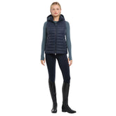 Eine Reiterin im kompletten LeMieux Reitoutfit bereit für den Sattel. Die navy  LeMieux Steppweste Rose wird hier stilvoll kombiniert und zeigt sich als vielseitiges Essential für den Reitsport. Das Bild vermittelt die perfekte Passform und Eleganz der Pufferweste in Aktion am Pferd. Hochwertige Reiterbekleidung für Damen, die Funktionalität im Stall mit einem modernen Look verbindet. Ideal als Inspiration für ein abgestimmtes Outfit im klassischen LeMieux-Stil.